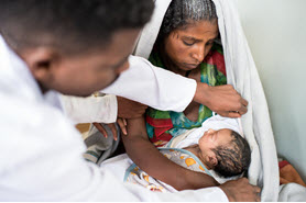 Mother holding an infant who is being examined.
